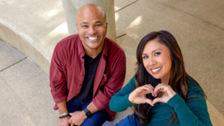 a man and woman smiling making a heart shape with her hands